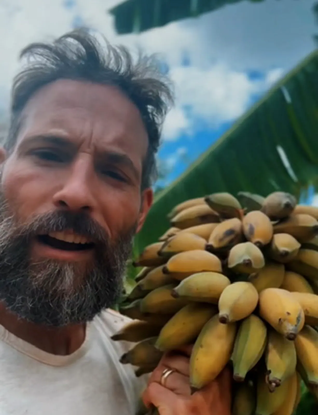 Matthew Nadu holding a large hand of ripe bananas from the backyard