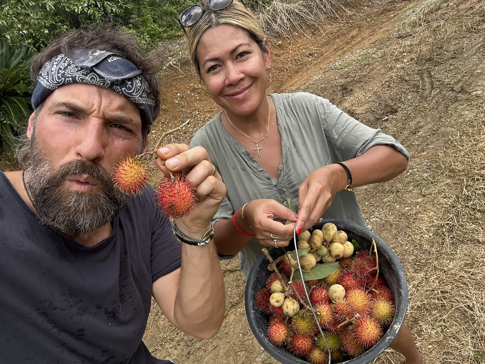 Matthew Nadu holding red rambutan beside a grower with a bucket of fresh-picked fruit