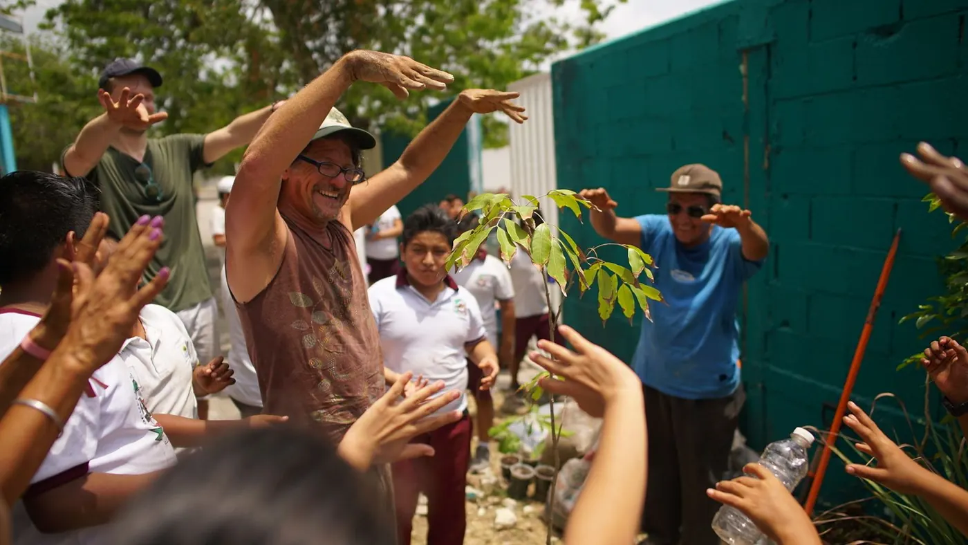 Students and volunteers cheering around a newly planted fruit tree at a school build day